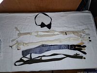 All three items laid out: bow tie top, beige and blue suspenders below