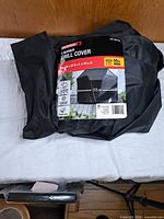 Folded black grill cover in original packaging with label showing brand and product info