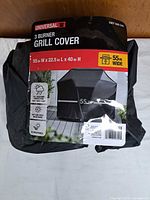 Retail-packaged Universal 3-burner grill cover showing dimensions and features