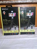 Front view of two sealed Vivitar Wireless Dual LED Lights Selfie Stick Tripod boxes