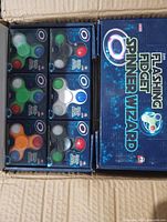 Open display box showing eight blister-packed fidget spinners in assorted colours inside retail packaging