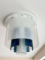 Chandelier mounted to ceiling showing frosted outer glass and darker inner glass, white canopy visible