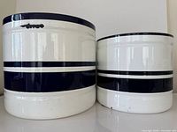 Front view of both enamel plant pots showing stripe decoration and large chip on rim of larger pot