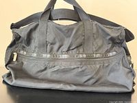 Front view of black nylon duffle showing logo ribbon, handles, overall condition