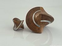 Both inlaid wood kinetic sculptures side by side on reflective surface