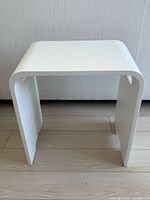 Front view of white molded resin stool showing curved top and overall shape