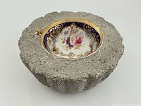 Top view showing porcelain teacup set into stone bowl, floral interior, gold rim, small gold bird accent