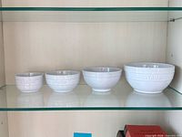 Four white ceramic bowls stacked on shelf, shows full set