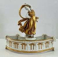 Front view showing curved base, gilt columns, ram heads, and gilded dancer