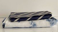 Both folded tablecloths stacked: navy striped plastic on top, blue tie-dye linen beneath