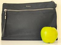Front view of black Tumi sling bag with apple for scale