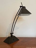 Front view of black metal desk lamp showing pyramid base, telescopic arm, and shade