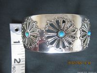 Top view of cuff showing three floral medallions with blue stones, ruler for scale