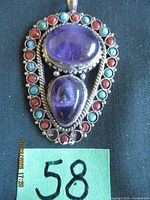 Front view of pendant showing two amethyst cabochons and surrounding small red and turquoise cabochons with bail visible
