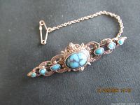 Front view of sterling silver brooch with turquoise stones and safety chain
