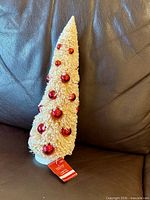 Full view of cream bottle brush tree with red ornaments and tag
