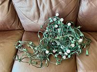 Tangled green-wire Christmas light strands with white round bulbs shown on brown couch