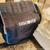 Overall view of Discover branded black messenger bag showing flap, logo, shoulder strap, and side accents