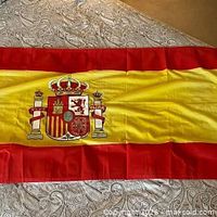 Full view of the Spanish flag laid flat showing colors and coat of arms