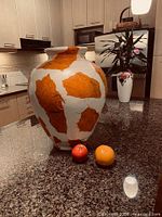 Full view of ceramic vase on countertop beside fruit for scale