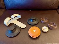 All seven utility items laid out: T-shaped bracket, two black suction pads, orange disk, beige suction pad, two brown spiral holders