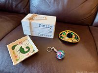 All four decorative items arranged on brown leather surface: wood book stack, miniature sombrero, ceramic dish, maraca keychain