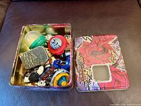 Open Yu-Gi-Oh tin showing assorted small toy parts and collectibles, lid alongside