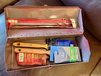 Interior view of toolbox showing paint brushes in sleeves and packaged drill bit
