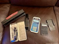 All items laid out on sofa: calculators, staplers, X-Acto trimmer, Staedtler compass set
