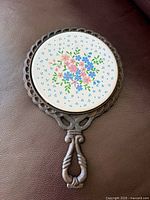 Full view of trivet showing cast iron frame, handle and floral ceramic center