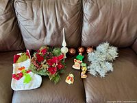 Group shot of all items on couch: stocking, wreath, tree topper, ball ornaments, small ornaments, tinsel
