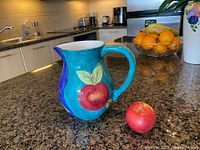 Left side view showing turquoise panel with red apple motif, pitcher spout and handle