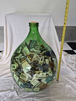 Full view of green glass bottle filled with matchbooks beside measuring tape