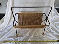 Front view of wicker magazine rack showing wicker basket and black metal frame with wood ball feet