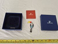 Brooch, open presentation box base, certificate booklet and box lid with logo displayed alongside measuring tape