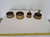 Top view of four brass ashtrays lined beside measuring tape