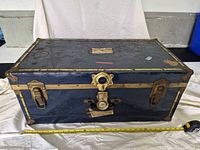Front exterior of trunk showing blue painted body, brass-tone banding, latches, central lock and measuring tape indicating length