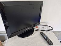 Front view of Samsung 19-inch TV on stand with remote and power cord