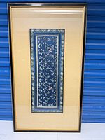 Full view of framed blue silk embroidery with beige mat and black frame