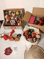 Overview of assorted glass and fabric ornaments in open boxes, cowbell ornaments, storage tin