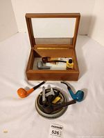 Overall view showing humidor open, ashtray, four pipes, tool and bottle