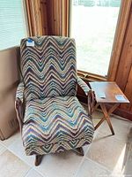 Armchair with chevron upholstery beside brown wood folding side table