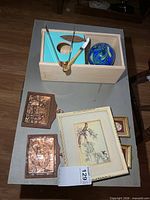 Overview of entire lot on table including crate with contents, copper plaques, framed print and mini frames