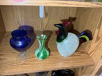 rooster figurine, green vase, blue goblet on shelf