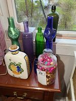 Group of assorted colored bottles, ceramic decanter and bead canister on table
