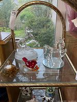 Group of four glass figurines on shelf: two clear glass horses, one red glass cardinal, one clear glass pyramid paperweight