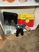 Overview of lot on shelf: records, binder, bottles, stocking stretcher, binoculars, matchbook items