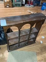 Front view of wooden wall shelf showing three tiers and arched supports