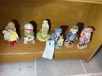 All six figurines lined on shelf with size reference tag