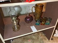All items grouped on shelf: oil lamp, hanging glass ball, amber boot pitcher, three boot shot glasses